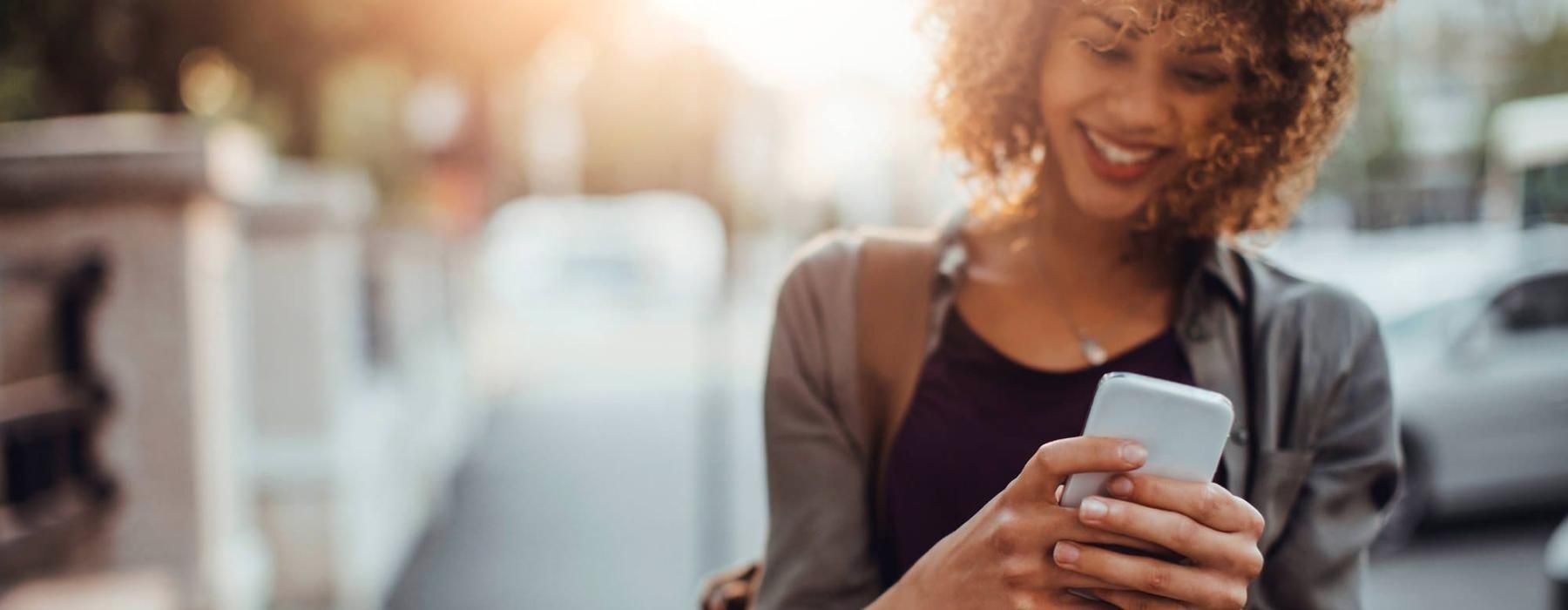 woman texts on her phone as she walks through the city