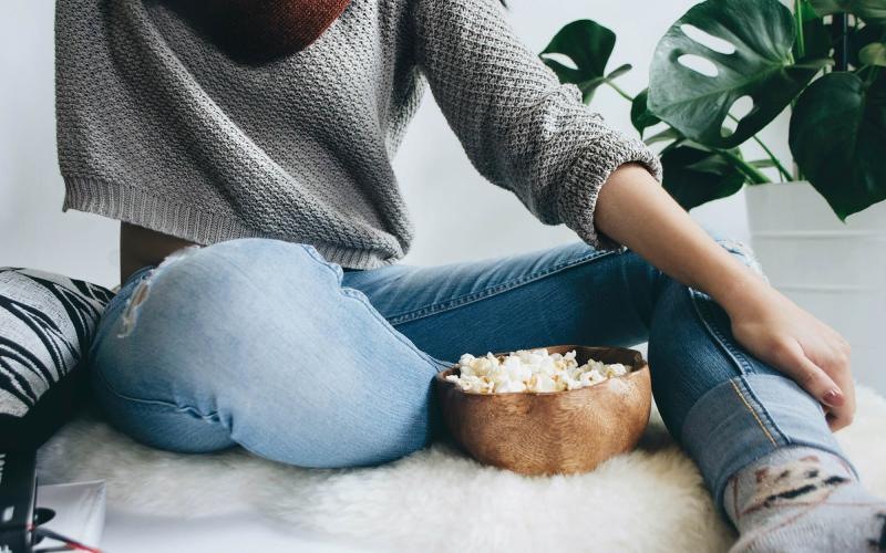 woman sits on a rug with a bowl of popcorn