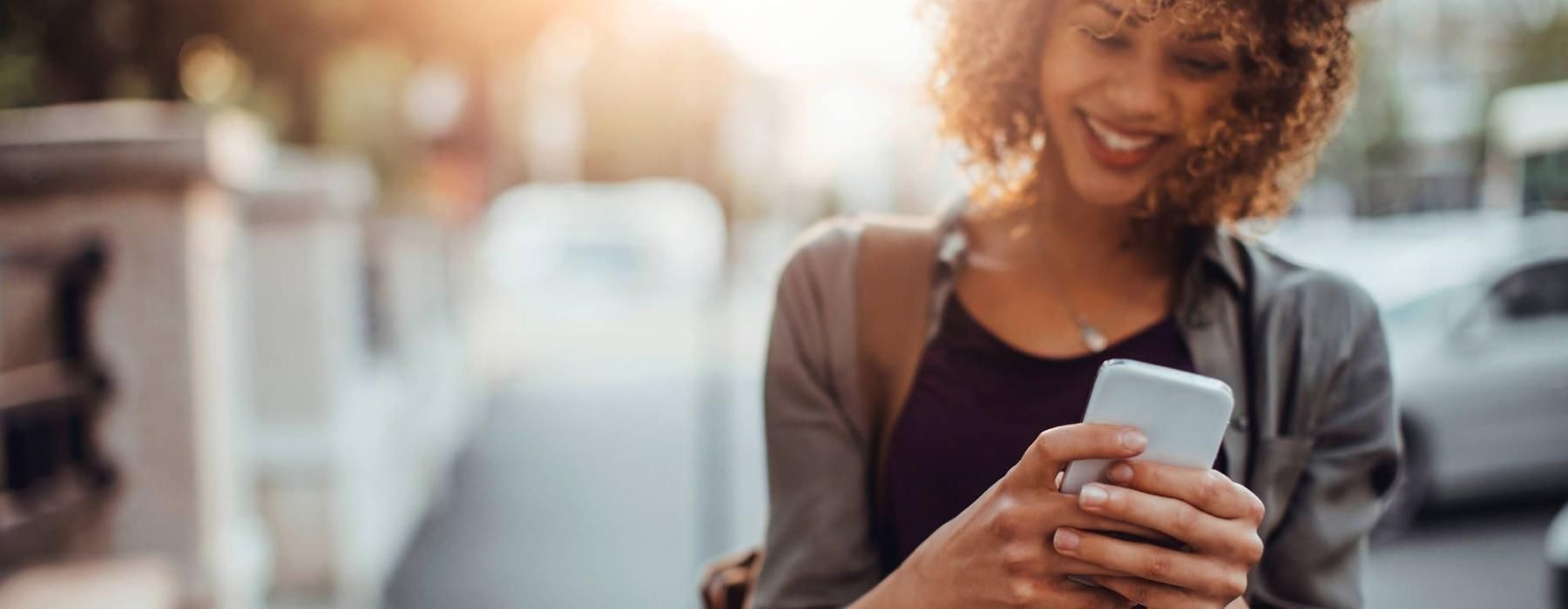 woman texts on her phone as she walks through the city